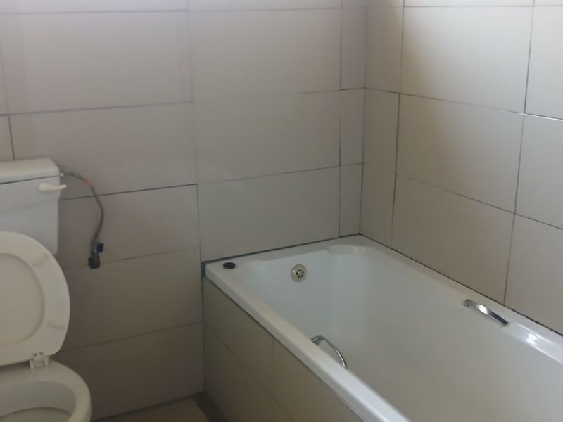 A functional bathroom featuring a standard bathtub and toilet with neutral wall tiling.