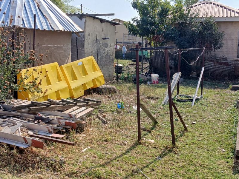 Rear yard area showing basic outbuildings with corrugated metal roofing and concrete foundation, requiring significant clearing and maintenance.