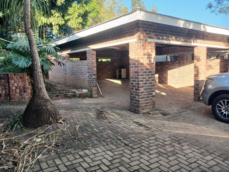 An open-sided face brick garage structure with a corrugated roof, situated on a paved driveway area.