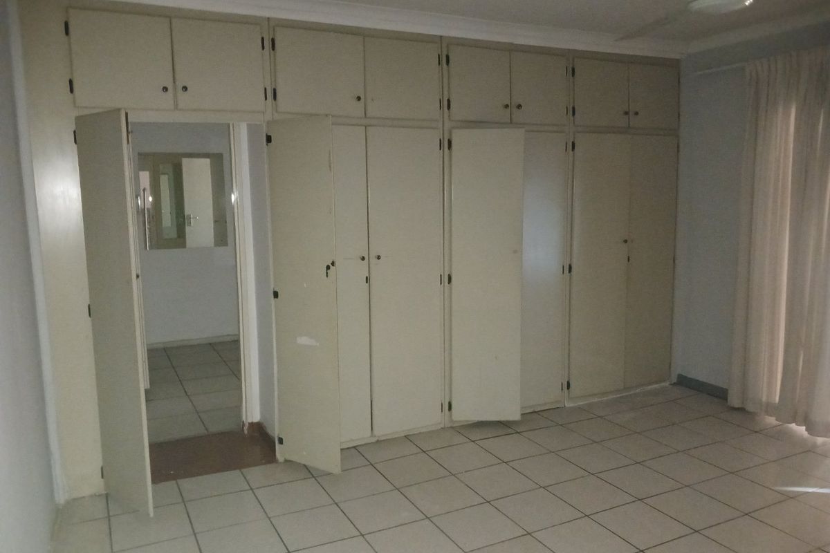 Spacious bedroom featuring extensive built-in cupboards, tiled flooring, and a ceiling fan, offering a blank canvas for renovation.