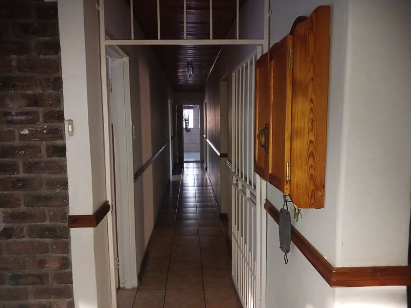 A long, narrow hallway featuring tiled flooring, a timber-paneled ceiling, and an exposed brick accent wall, leading towards the rear of the property.