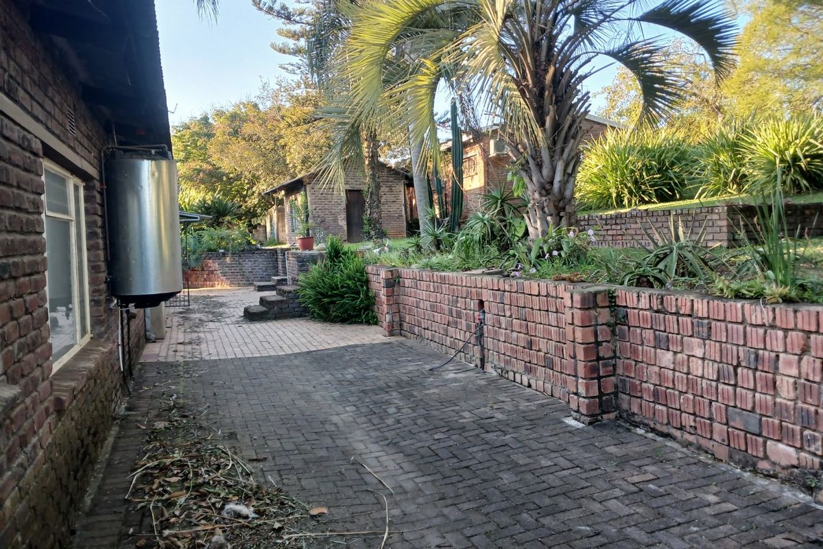 Rear exterior view featuring brick paved patio area, tiered brick retaining walls, and established garden landscaping.