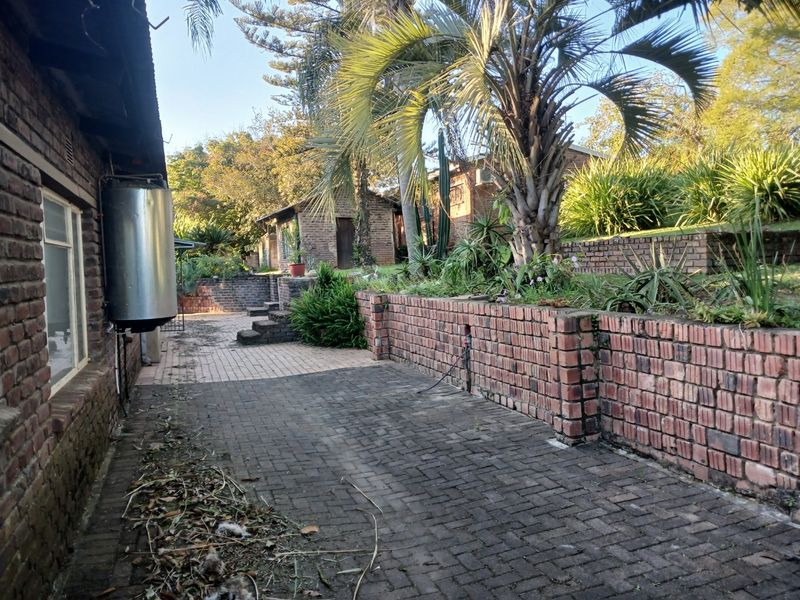 Rear exterior view featuring brick paved patio area, tiered brick retaining walls, and established garden landscaping.