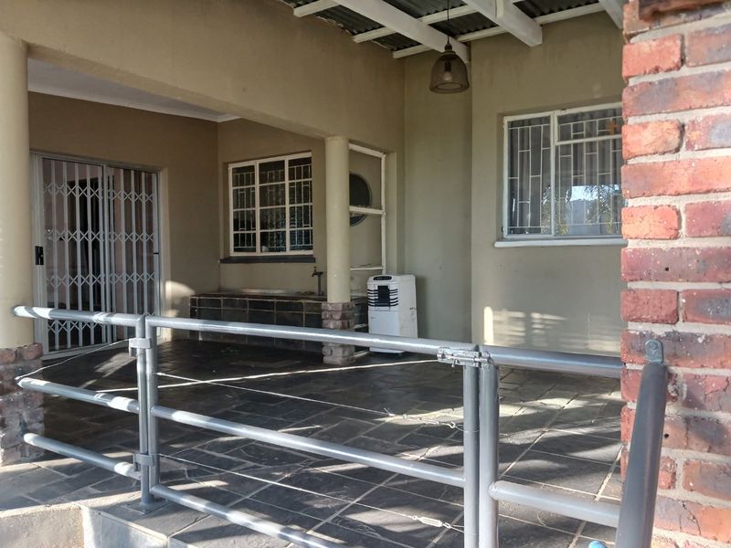 A covered patio area featuring slate tile flooring, a built-in counter, and metal security features, offering a functional outdoor space for relaxation.