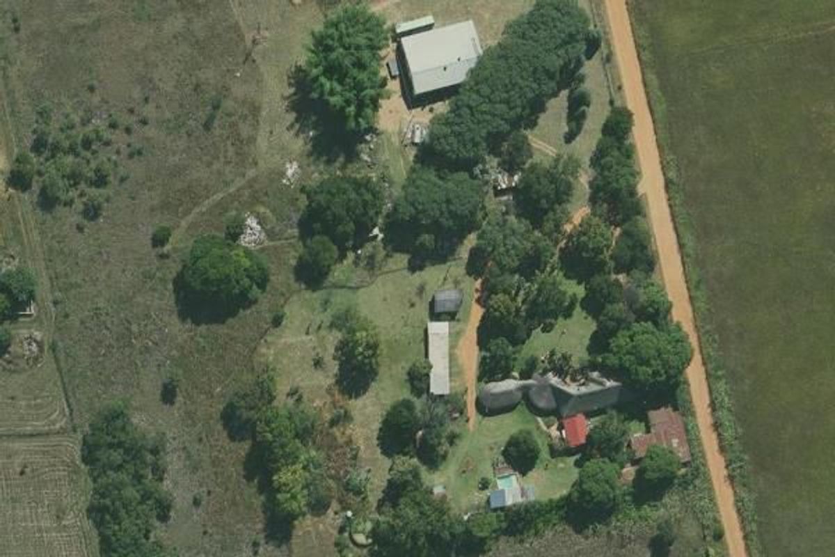 Aerial view of a farm property featuring a main residence with a thatched roof, swimming pool, outbuildings, and extensive surrounding grounds.