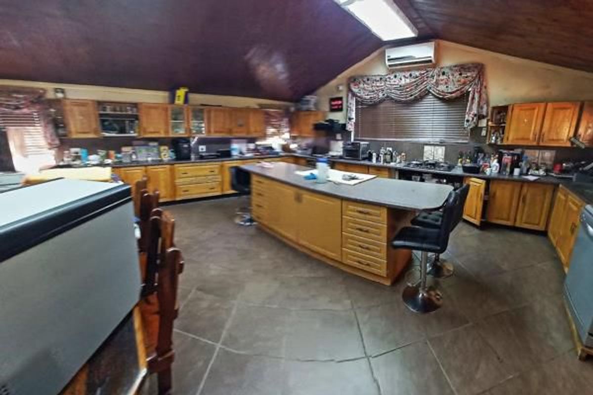 Spacious kitchen featuring extensive wooden cabinetry, a central island, vaulted timber ceilings, and tiled flooring, offering a functional layout with integrated cooking appliances.