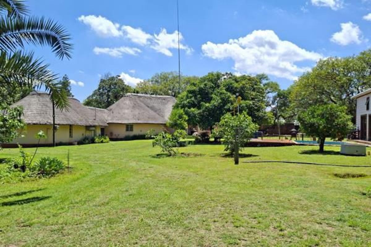 Spacious rear garden featuring a traditional thatch-roofed farmhouse, mature trees, and a swimming pool area set within a well-maintained lawn.