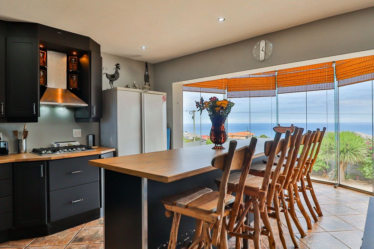 Modern kitchen featuring dark cabinetry, a wooden breakfast bar, and expansive glass sliding doors offering panoramic ocean views.