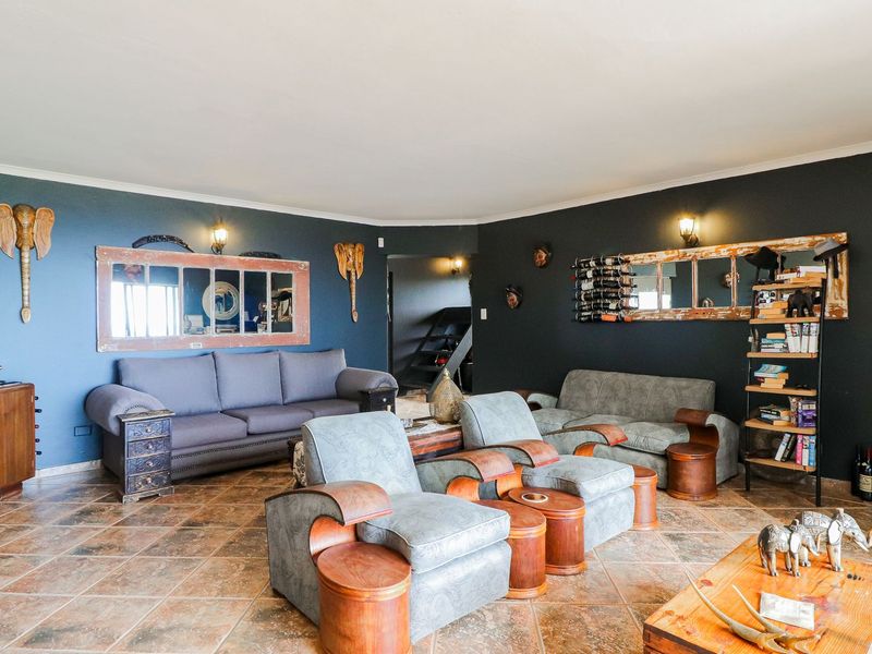 A spacious living room featuring dark painted walls, tiled flooring, and wall-mounted lighting fixtures, offering a comfortable and distinct atmosphere.