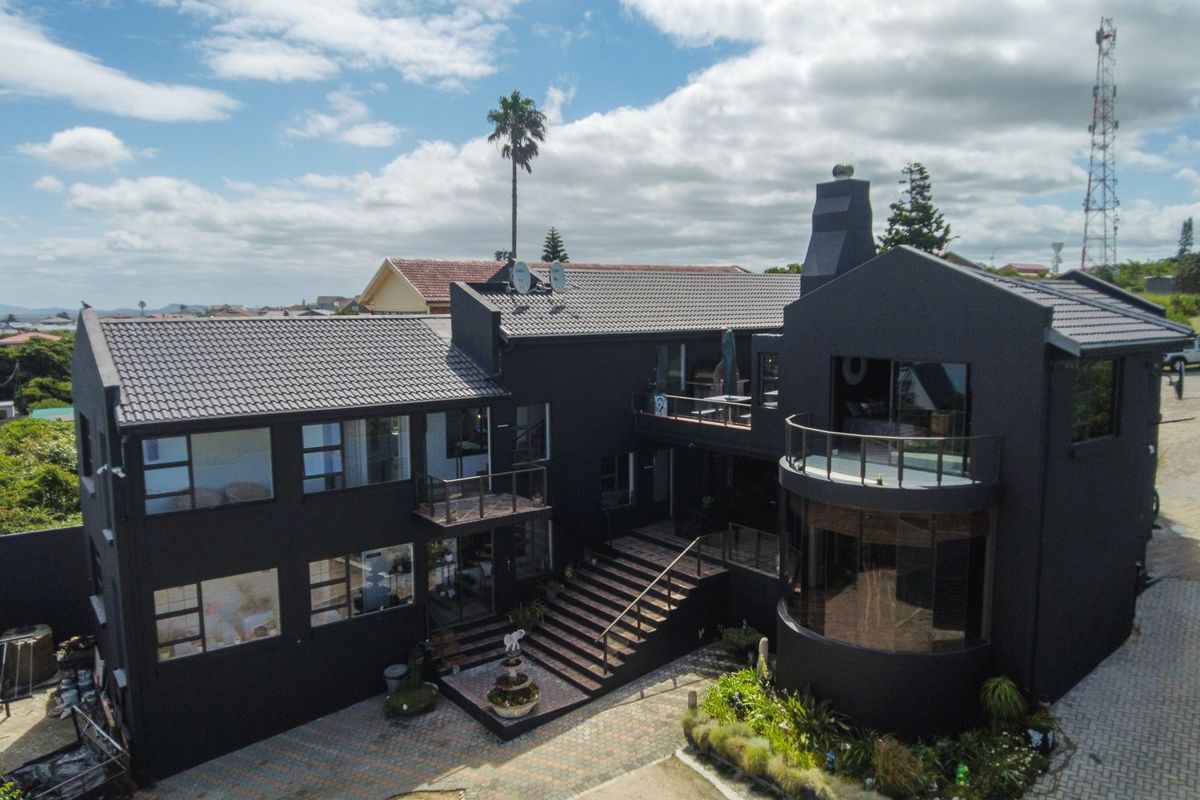 Aerial view of a modern multi-level residential property featuring a dark exterior finish, tiled roof, balconies, and a paved driveway.