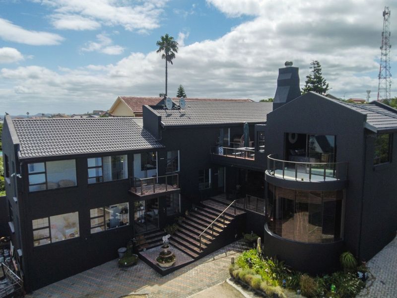 Aerial view of a modern multi-level residential property featuring a dark exterior finish, tiled roof, balconies, and a paved driveway.