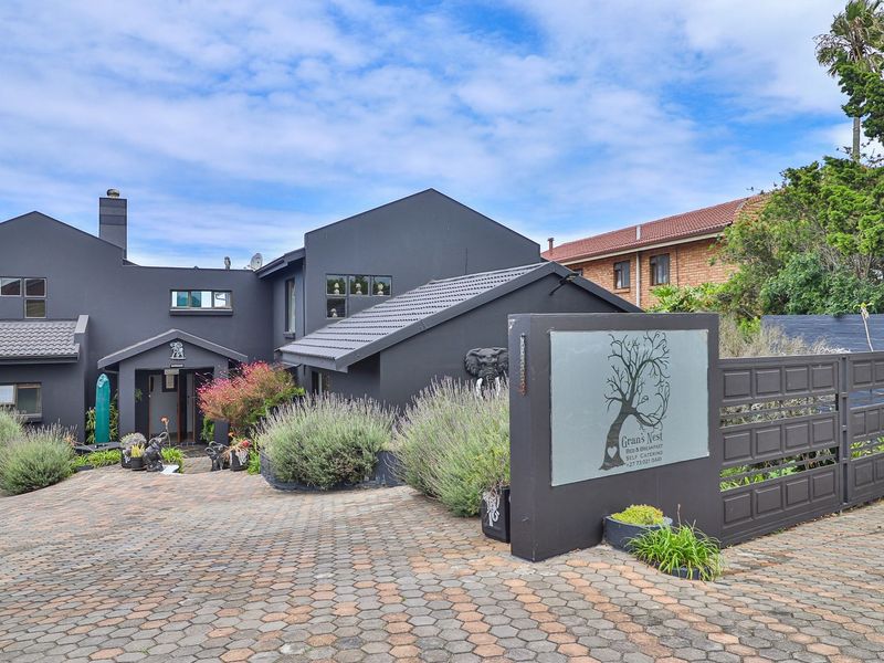 Front exterior view of a modern dark-painted house featuring a paved driveway, gated entrance, and established garden landscaping.