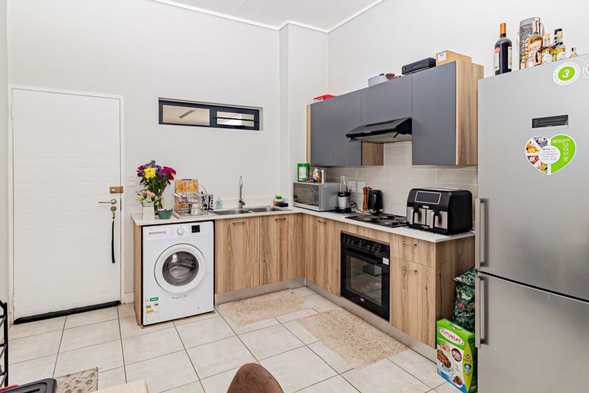 Modern kitchen featuring wood-finish cabinetry, integrated oven and hob, tiled flooring, and a dedicated space for a washing machine.