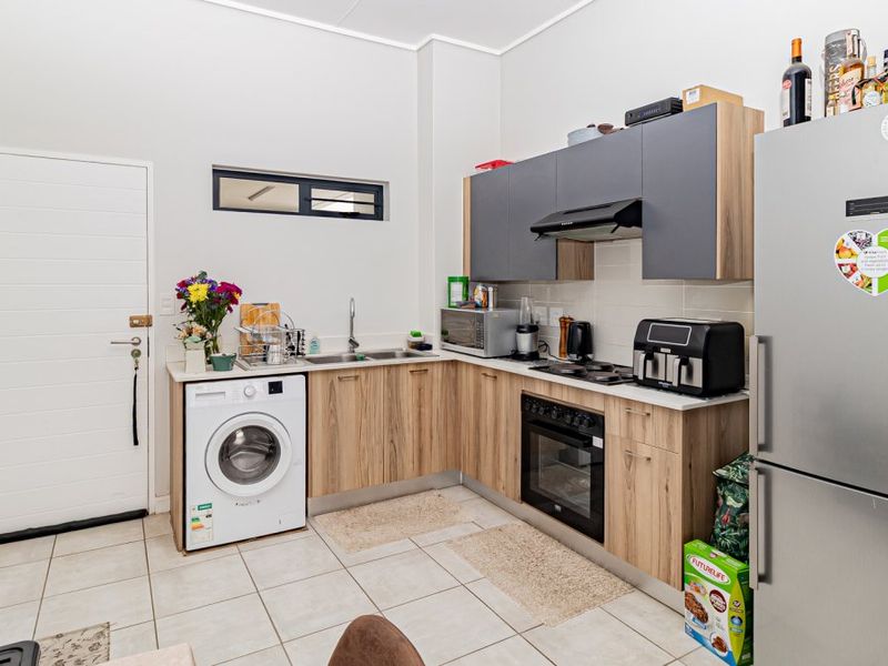 Modern kitchen featuring wood-finish cabinetry, integrated oven and hob, tiled flooring, and a dedicated space for a washing machine.