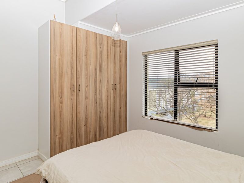 A bedroom featuring a built-in wood-finish wardrobe, tiled flooring, and a window with venetian blinds.