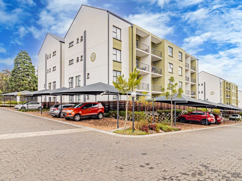 Exterior view of a modern multi-story apartment complex featuring paved parking areas with covered bays and private balconies.
