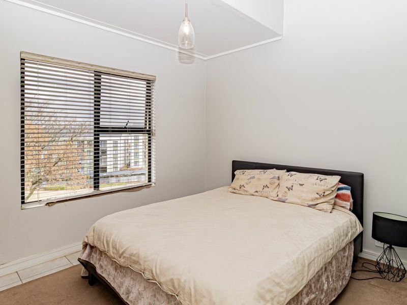 A bedroom featuring neutral walls, carpeted flooring, and a window fitted with venetian blinds, providing natural light and a view of the surrounding area.