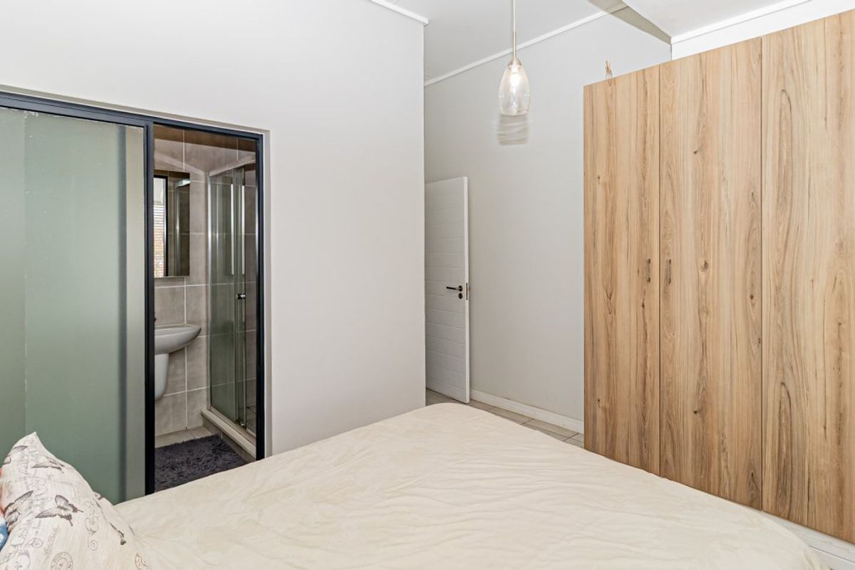 A well-maintained bedroom featuring a large built-in wooden wardrobe and an integrated en-suite bathroom with a glass shower enclosure and pedestal basin.