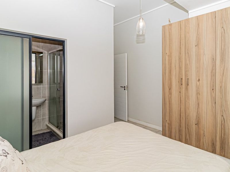 A well-maintained bedroom featuring a large built-in wooden wardrobe and an integrated en-suite bathroom with a glass shower enclosure and pedestal basin.