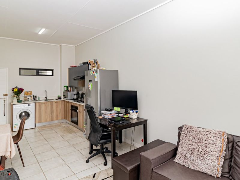 Open-plan living area featuring a compact kitchen with built-in cabinetry, oven, and extractor fan, finished with neutral tiled flooring throughout.