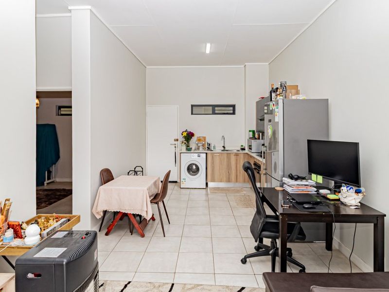 Open-plan living area featuring tiled flooring and a functional kitchen space with built-in cabinetry and laundry plumbing connections.