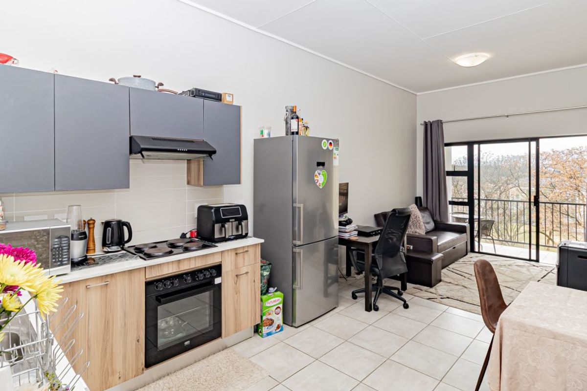 Open-plan living area featuring a modern kitchen with built-in cabinetry, electric hob, and oven, leading to a balcony through sliding glass doors.