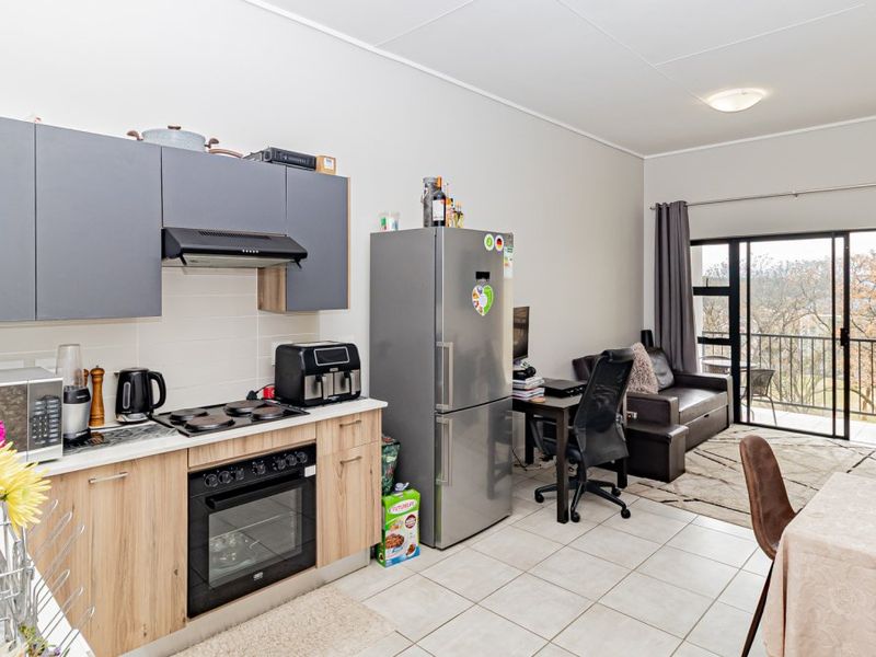 Open-plan living area featuring a modern kitchen with built-in cabinetry, electric hob, and oven, leading to a balcony through sliding glass doors.