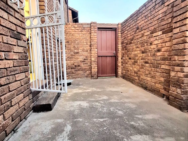 A private rear courtyard area featuring exposed brick walls, concrete flooring, and a secure access door.