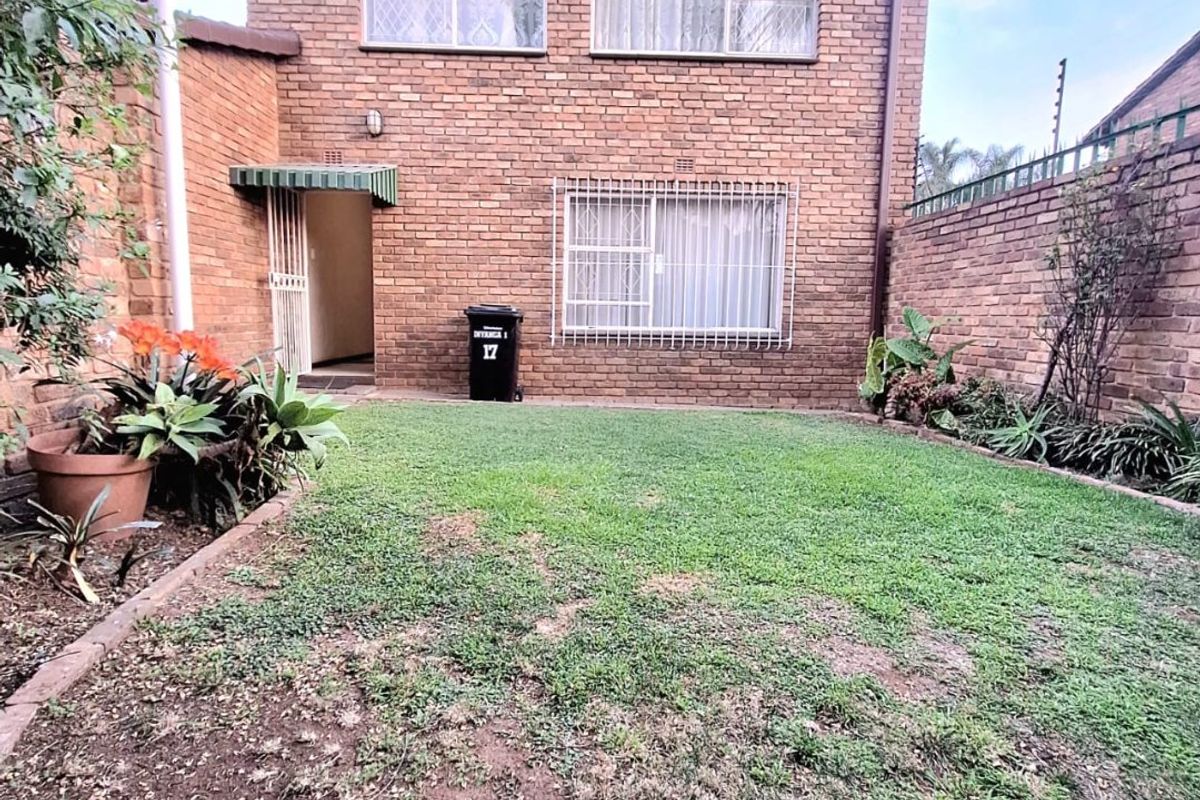 Rear view of a brick townhouse featuring a private garden area with a lawn and secure window bars.