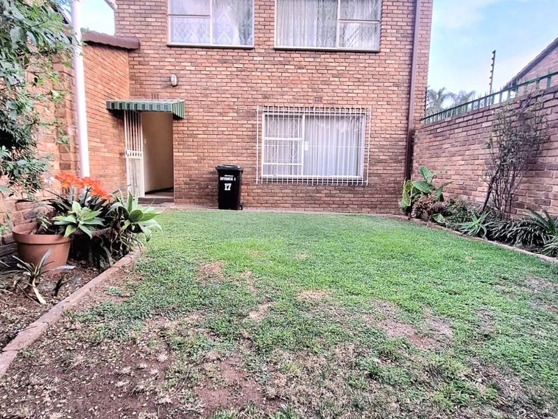 Rear view of a brick townhouse featuring a private garden area with a lawn and secure window bars.