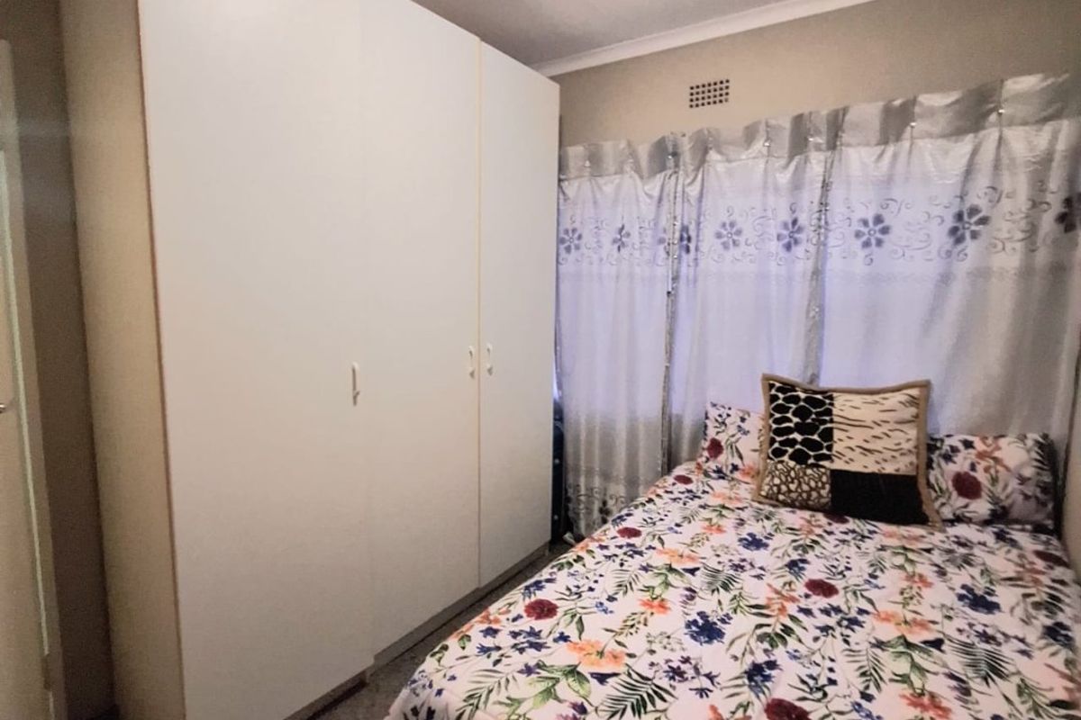 A bedroom featuring a large white built-in wardrobe, neutral wall finishes, and a ventilation grille.