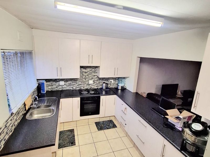 A functional kitchen featuring white cabinetry, dark laminate countertops, a built-in oven with hob, and tiled flooring with a mosaic backsplash.