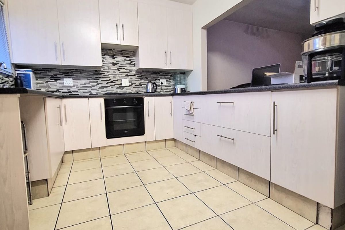 A functional kitchen featuring light-toned cabinetry, a mosaic tile backsplash, built-in oven, and ceramic floor tiles with a convenient pass-through opening.