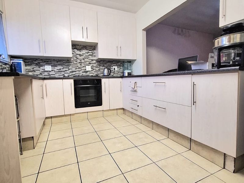 A functional kitchen featuring light-toned cabinetry, a mosaic tile backsplash, built-in oven, and ceramic floor tiles with a convenient pass-through opening.