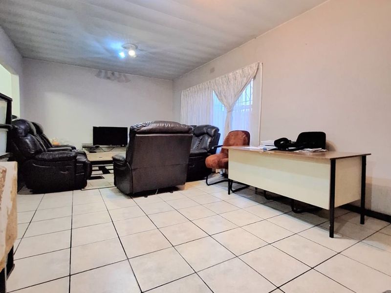 Spacious living area featuring neutral tiled flooring and large windows with curtain rails, offering a versatile layout for lounge and home office use.