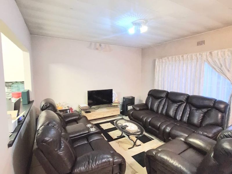 A living room featuring tiled flooring and a neutral wall finish, with an open-plan layout connecting to the adjacent kitchen area.