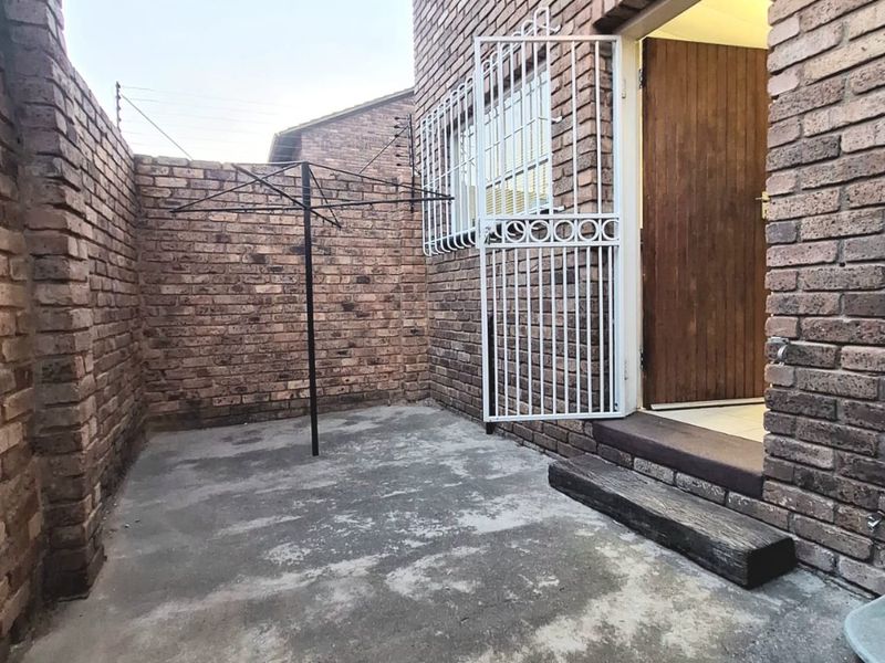 A private rear courtyard area featuring exposed brick walls, a concrete patio surface, and a secure entrance gate leading into the townhouse.