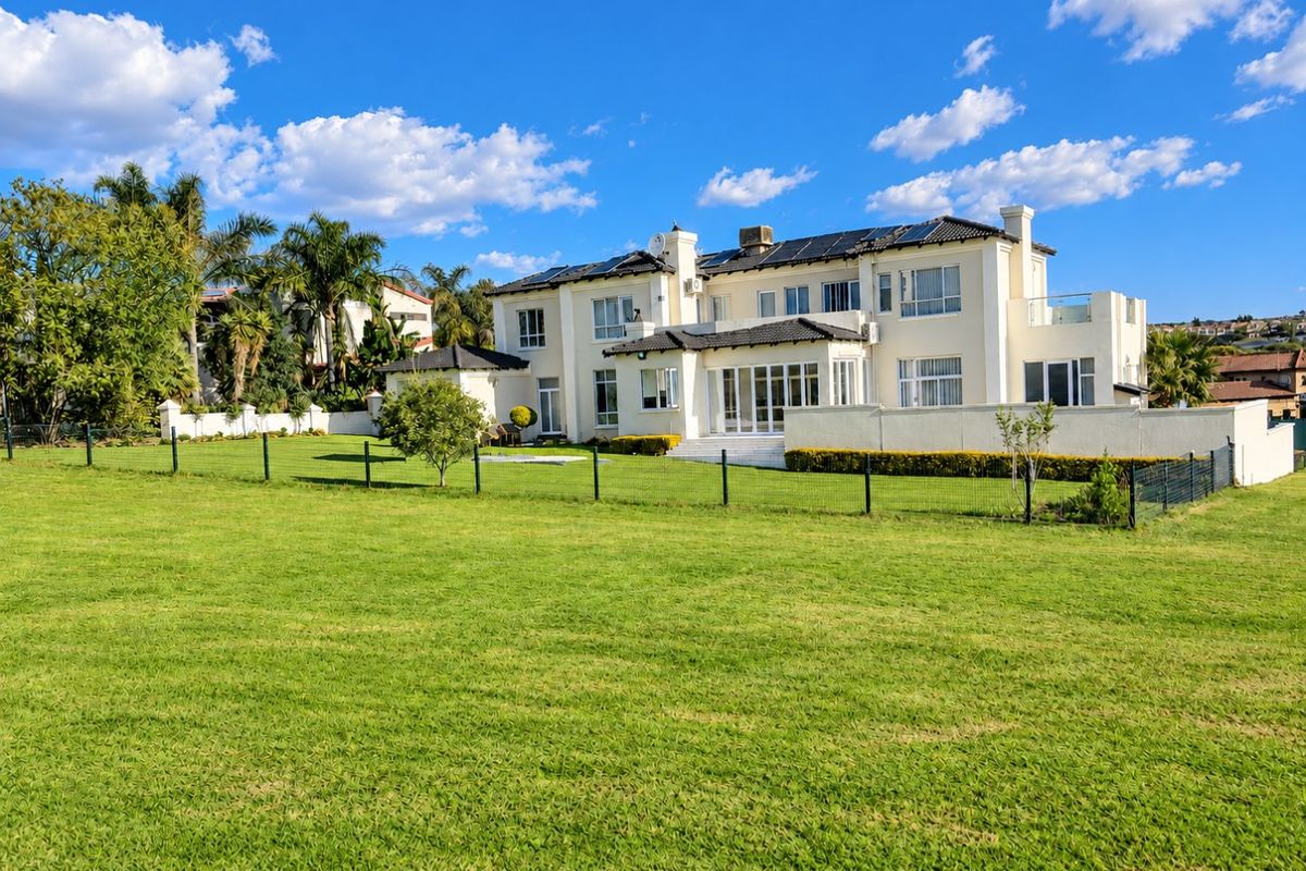 A spacious rear view of a large multi-story residence featuring a well-maintained lawn, solar panels, and a balcony.