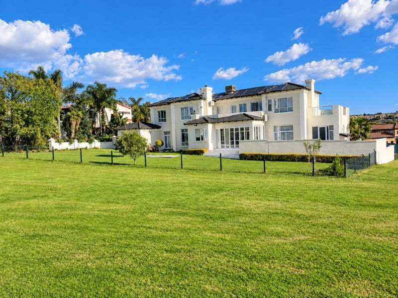 A spacious rear view of a large multi-story residence featuring a well-maintained lawn, solar panels, and a balcony.
