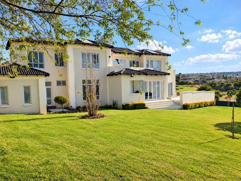 Rear view of a double-story residence featuring a tiled roof with solar panels, expansive lawn, and a paved patio area overlooking the estate.