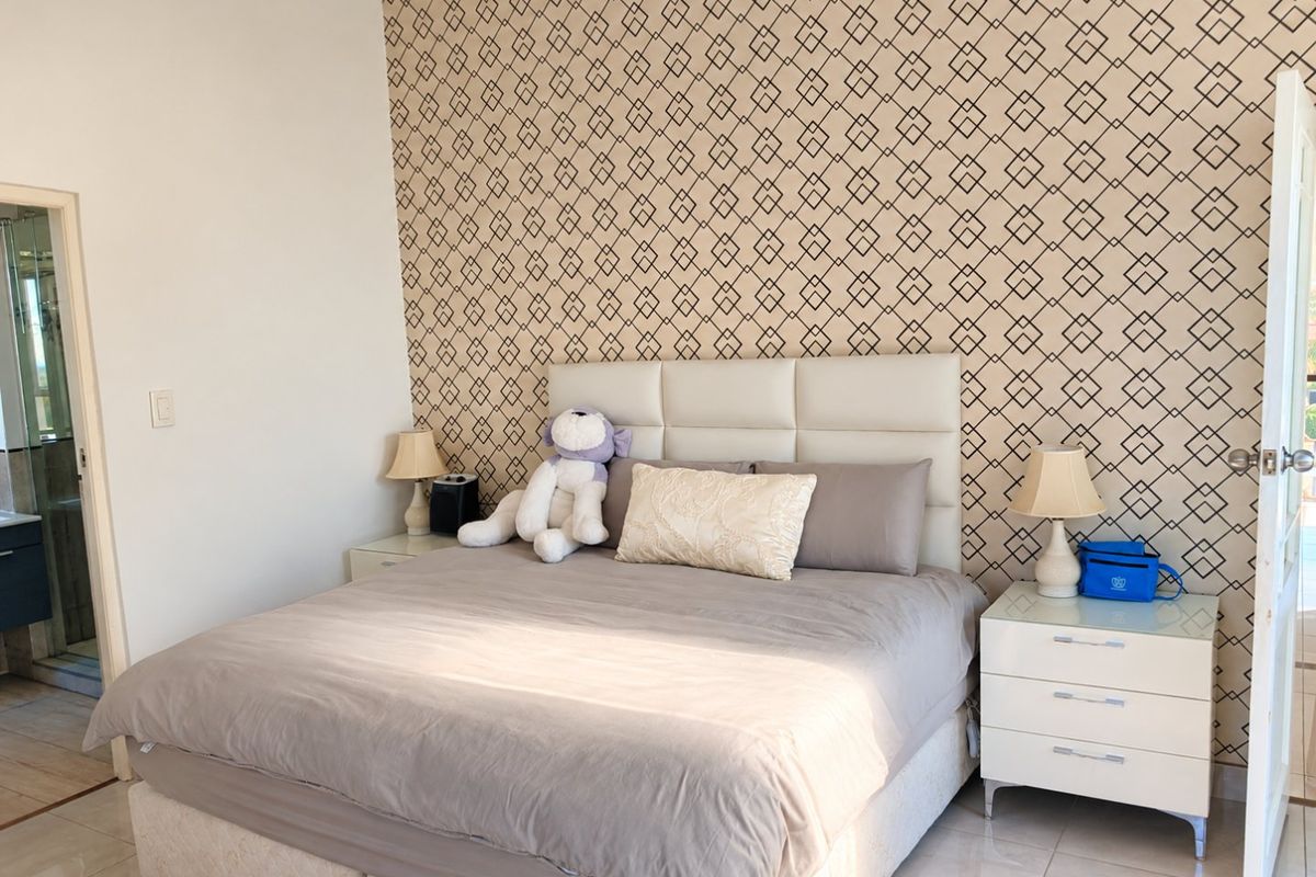 A well-maintained bedroom featuring patterned wallpaper, tiled flooring, and direct access to an en-suite bathroom.