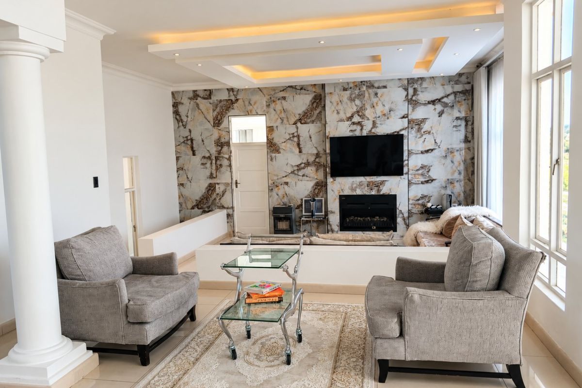Spacious living room featuring a striking marble-look feature wall, built-in fireplace, recessed ceiling with ambient cove lighting, and large windows.