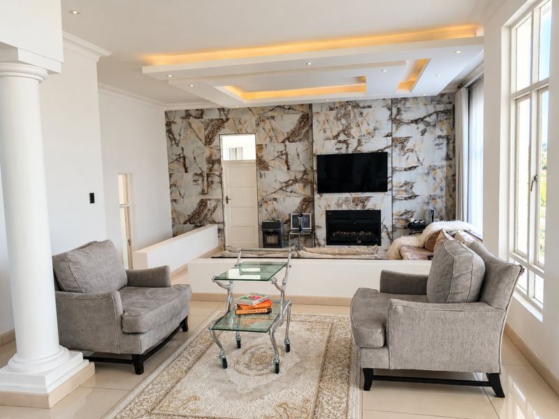 Spacious living room featuring a striking marble-look feature wall, built-in fireplace, recessed ceiling with ambient cove lighting, and large windows.