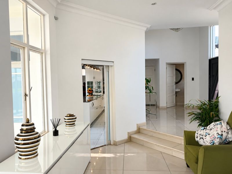 A bright, tiled hallway featuring crown molding, recessed lighting, and a sliding door providing a view into the kitchen area.