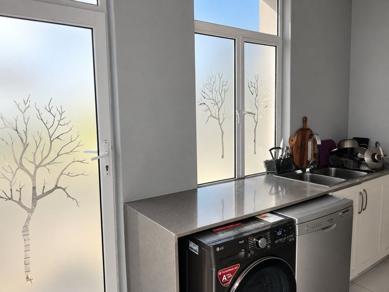 A functional laundry area featuring stone countertops, a stainless steel sink, and modern cabinetry with natural light through frosted glass windows and a door.