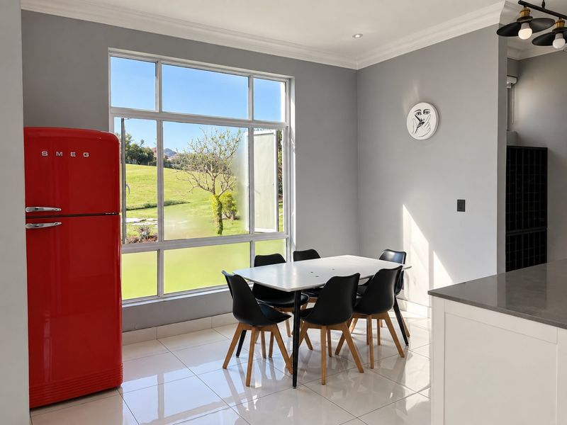 Bright open-plan dining area featuring large windows with garden views, sleek tiled flooring, and modern finishes, seamlessly connected to the kitchen space.
