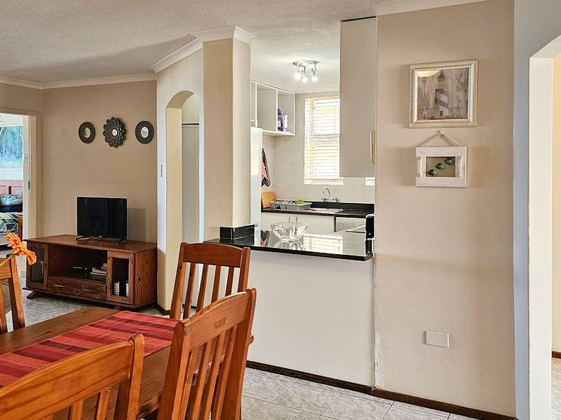 Open-plan living and dining area featuring a functional kitchen with granite countertops and tiled flooring, with a view into the adjacent bathroom.