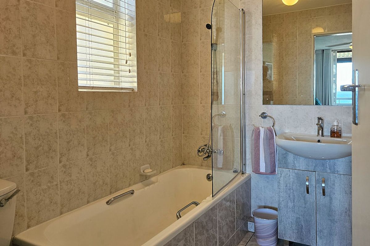 A functional bathroom featuring a bathtub with a glass shower screen, a vanity unit with a basin, and neutral wall tiling.