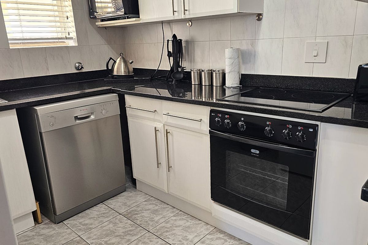 A functional kitchen featuring white cabinetry, black granite countertops, a built-in oven, electric hob, and tiled finishes throughout.