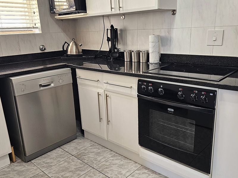 A functional kitchen featuring white cabinetry, black granite countertops, a built-in oven, electric hob, and tiled finishes throughout.